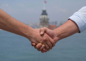 İstanbul'da Kız Kulesi manzarası önünde tokalaşan iki kişinin elleri.