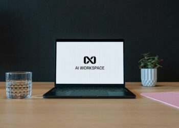Masada duran laptop ekranında AI WORKSPACE yazısı ve yandaki bardak