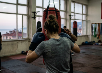 Salonda boks antrenmanı yapan sporcuların arkadan görünümü ve büyük bir Türk bayrağı.