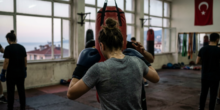 Salonda boks antrenmanı yapan sporcuların arkadan görünümü ve büyük bir Türk bayrağı.