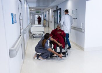 Hastane koridorunda yürüyen doktorlar ve tekerlekli sandalyedeki hasta.