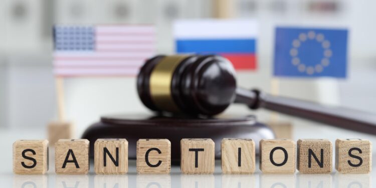 Ahşap harflerle yazılmış sanctions yazısı arkasında küçük bayraklar ve tokmak duruyor.