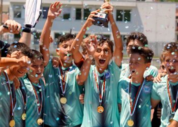 Kupa kaldıran ve madalya takan genç futbolcular konfeti yağmuru altında sevinç yaşıyor.