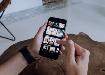Ahşap masa üzerinde telefonla dijital yayın platformu katalog inceleyen kişi.