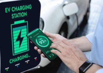 Şarj istasyonunda elektrikli otomobilini telefon uygulamasıyla şarj eden bir kişi.
