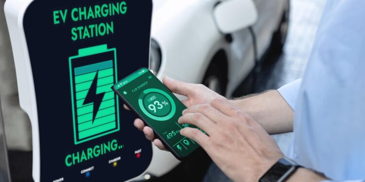 Şarj istasyonunda elektrikli otomobilini telefon uygulamasıyla şarj eden bir kişi.