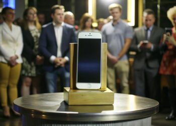 Masada sergilenen beyaz akıllı telefonun arkasında etkinlik izleyen kalabalık bulunuyor.