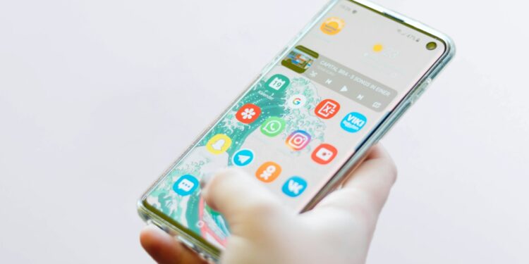 Şeffaf kılıflı bir akıllı telefon tutan kişinin ekranındaki uygulama simgeleri.