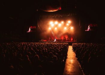 Kırmızı sahne ışıkları altında konser izleyen kalabalık kitle.
