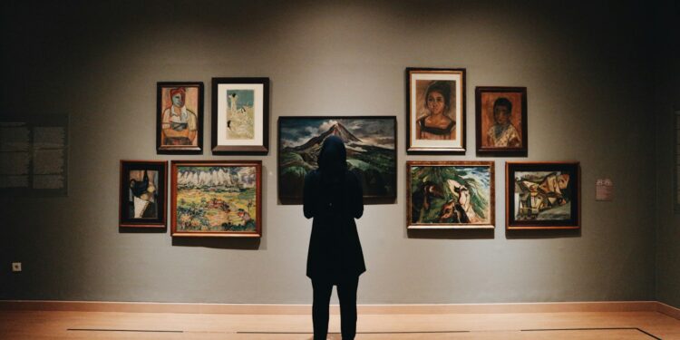 Sanat galerisinde duvardaki tablolara bakan tesettürlü bir ziyaretçi.