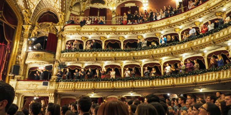 Tarihi bir opera binasının ihtişamlı salonunda alkış tutan kalabalık izleyiciler.