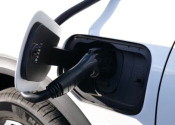 Şarj istasyonunda elektrikli bir araca bağlanmış siyah şarj kablosu ve kapağı.