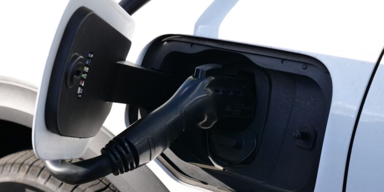 Şarj istasyonunda elektrikli bir araca bağlanmış siyah şarj kablosu ve kapağı.