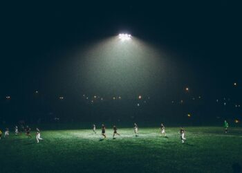 Gece saatlerinde stadyumda aydınlatma altında futbol maçı oynayan oyuncular.