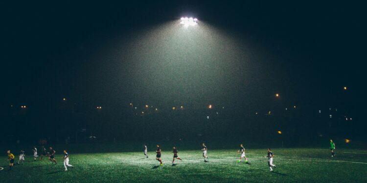 Gece saatlerinde stadyumda aydınlatma altında futbol maçı oynayan oyuncular.