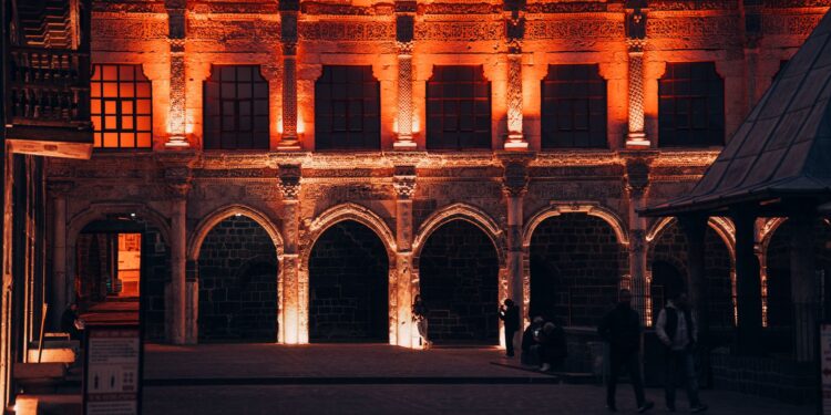 Gece ışıklandırılmış tarihi taş binanın avlusu ve kemerli sütunları.