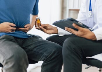 Mide ağrısı çeken bir hastaya doktor ilaç şişesi uzatıyor.