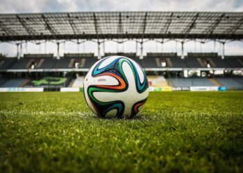 Çim saha üzerinde duran renkli futbol topu ve arka planda tribünler.