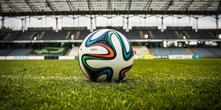 Çim saha üzerinde duran renkli futbol topu ve arka planda tribünler.