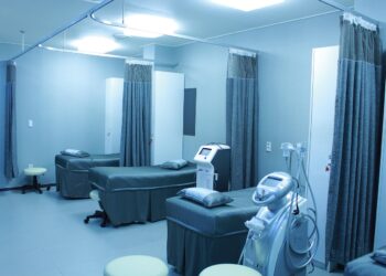 Hastane odasında yataklar, tıbbi cihazlar ve perdeler görünen steril bir klinik iç mekan çekimi.