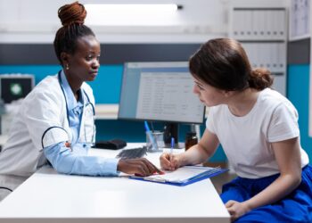 Doktor masada oturan hastaya bir belgeyi göstererek açıklama yapıyor.