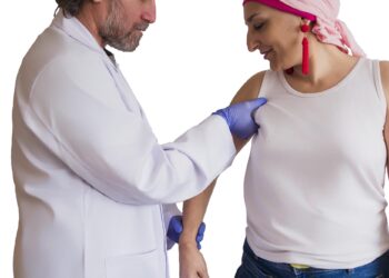 Bir doktor eldivenli eliyle hastanın omzunu ve kolunu muayene ediyor.