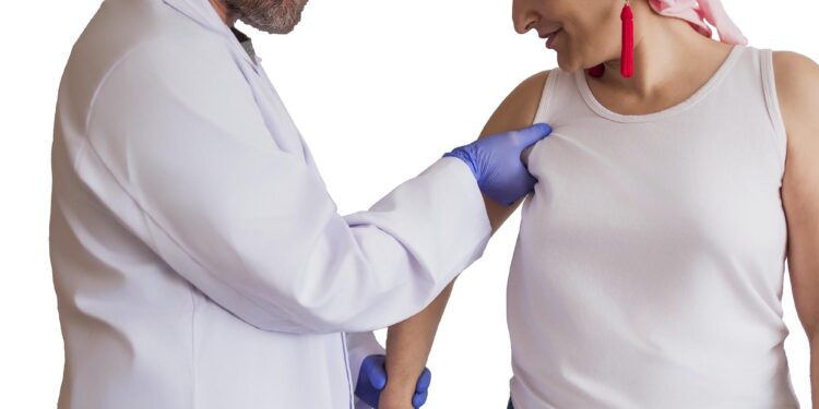 Bir doktor eldivenli eliyle hastanın omzunu ve kolunu muayene ediyor.