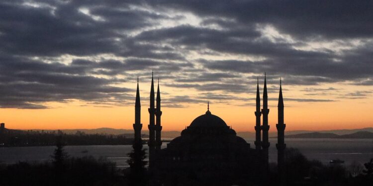 Gün batımında bulutlu gökyüzü altında İstanbul'un tarihi silueti ve minareleri görülüyor.