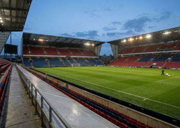 Futbol sahasında akşam saatlerinde bakım çalışması yapan bir görevli ve tribünler.