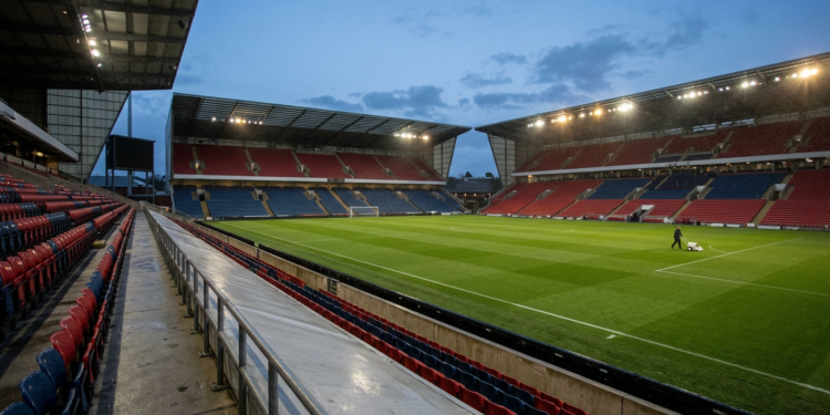 Futbol sahasında akşam saatlerinde bakım çalışması yapan bir görevli ve tribünler.