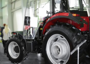 Fabrika ortamında kırmızı renkli modern bir traktörün ön tekerleği ve kabini
