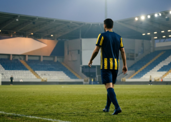 Futbol sahasında yürüyen sarı lacivert formalı oyuncunun arkadan görünümü.